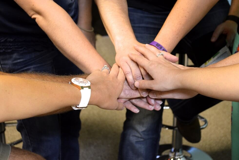 Six people stack their hands together in a gesture symbolizing teamwork and unity.