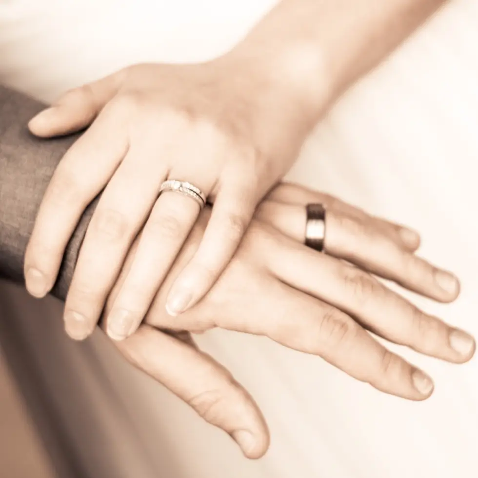 Two hands with wedding rings rest atop one another, symbolizing marriage or partnership.