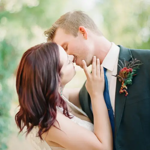 A couple in wedding attire embrace outdoors, sharing an intimate moment in soft natural light.
